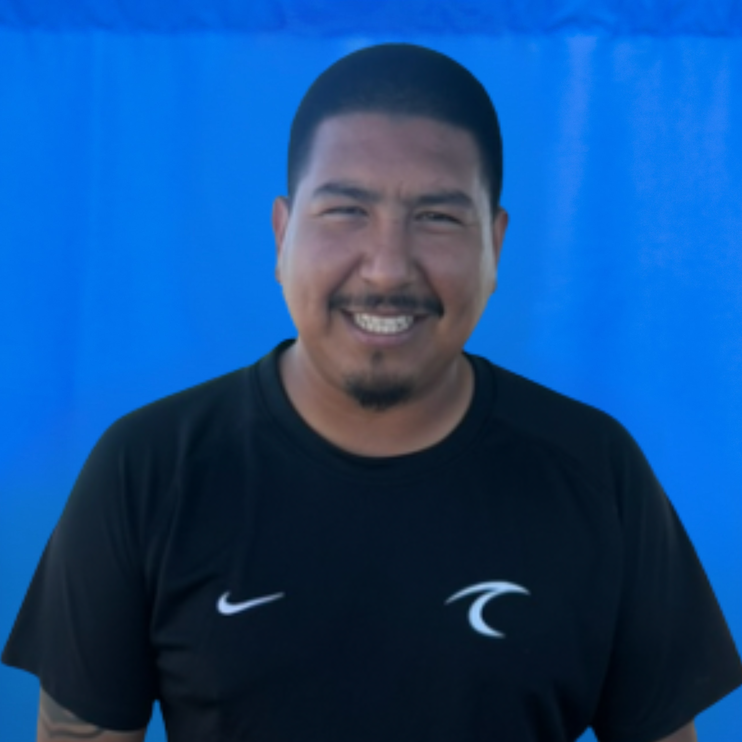 Anthony Hernandez Smiling man with short black hair and a goatee wearing a black T‑shirt, against a bright blue background.