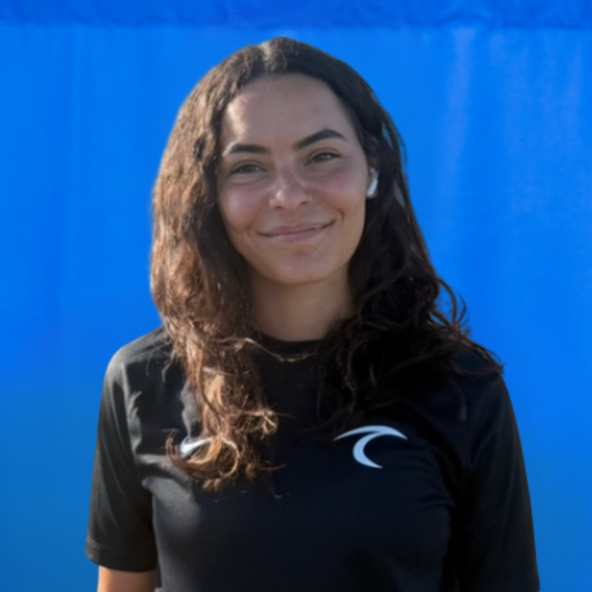 Casey Villa Smiling woman with long dark hair wearing a black shirt, against a bright blue background.